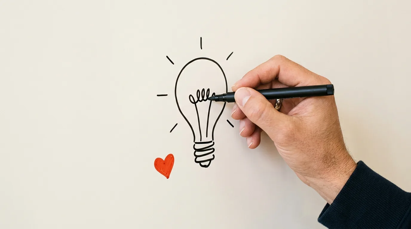 A hand sketching a lightbulb on a whiteboard with a marker